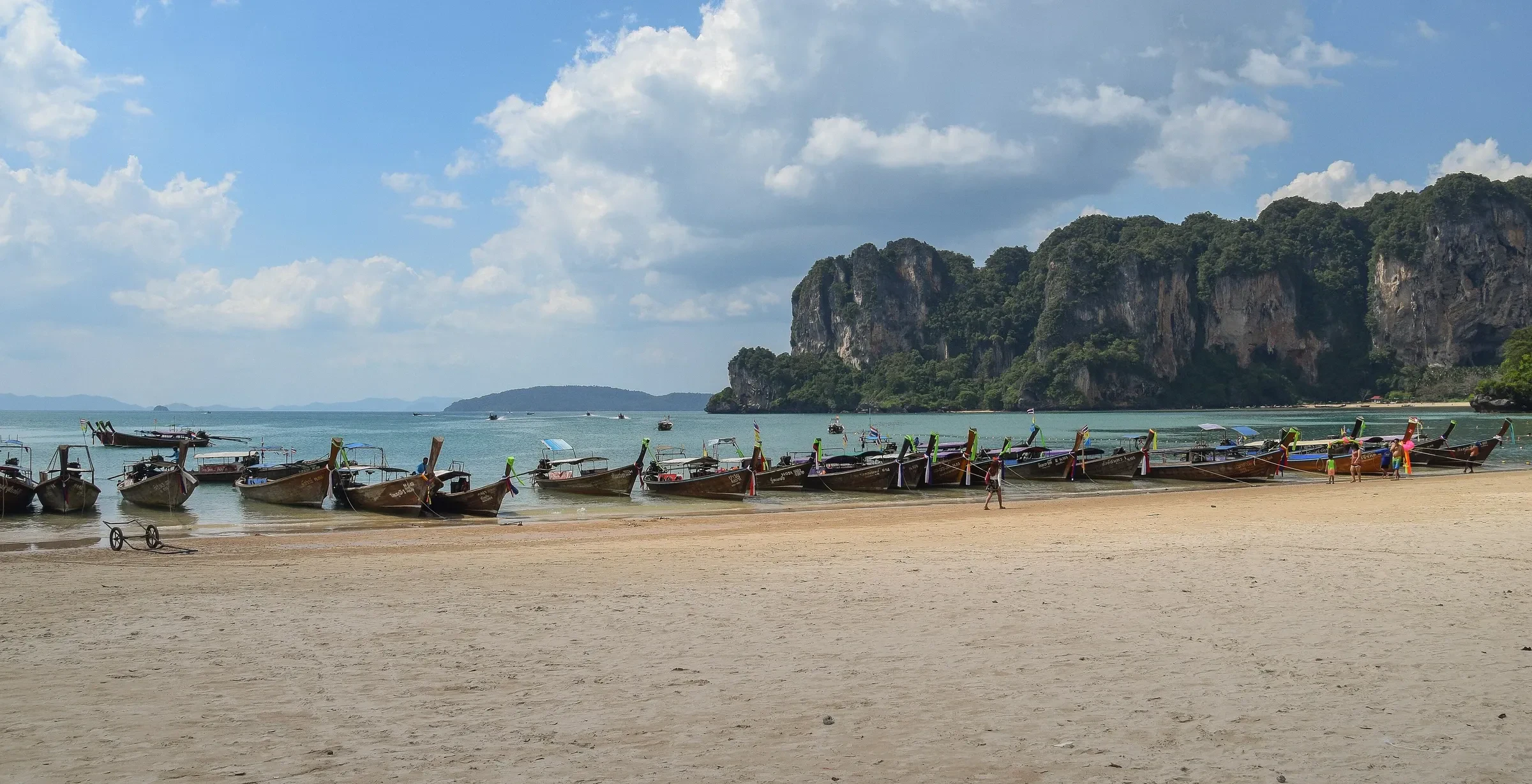 A line of longtail boats on the sand below the limestone cliffs of West Railay