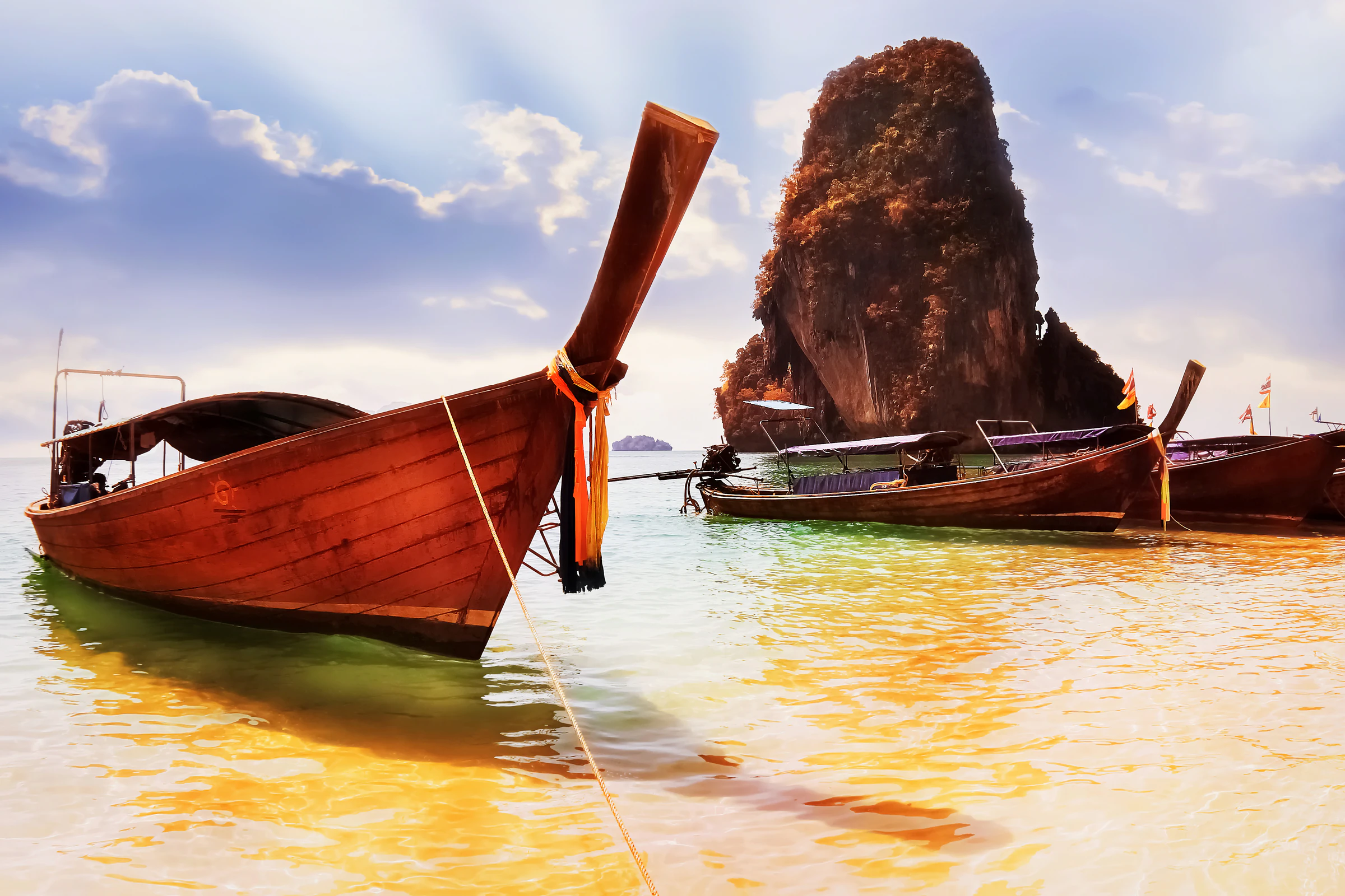 A traditional longtail boat pulled up on a beach below limestone cliffs