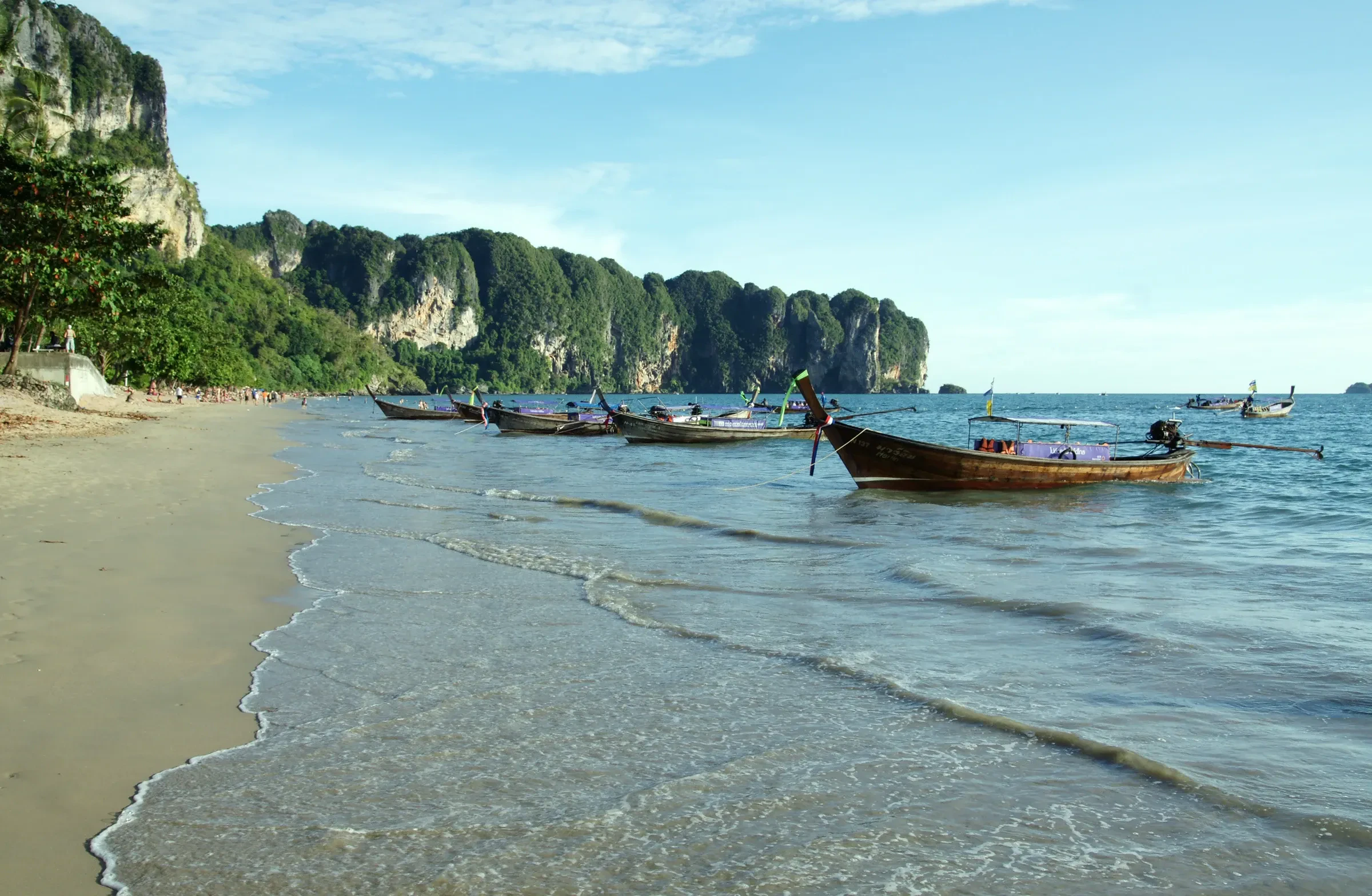 Longtail boats at the water's edge on Ao Nang beach below limestone cliffs