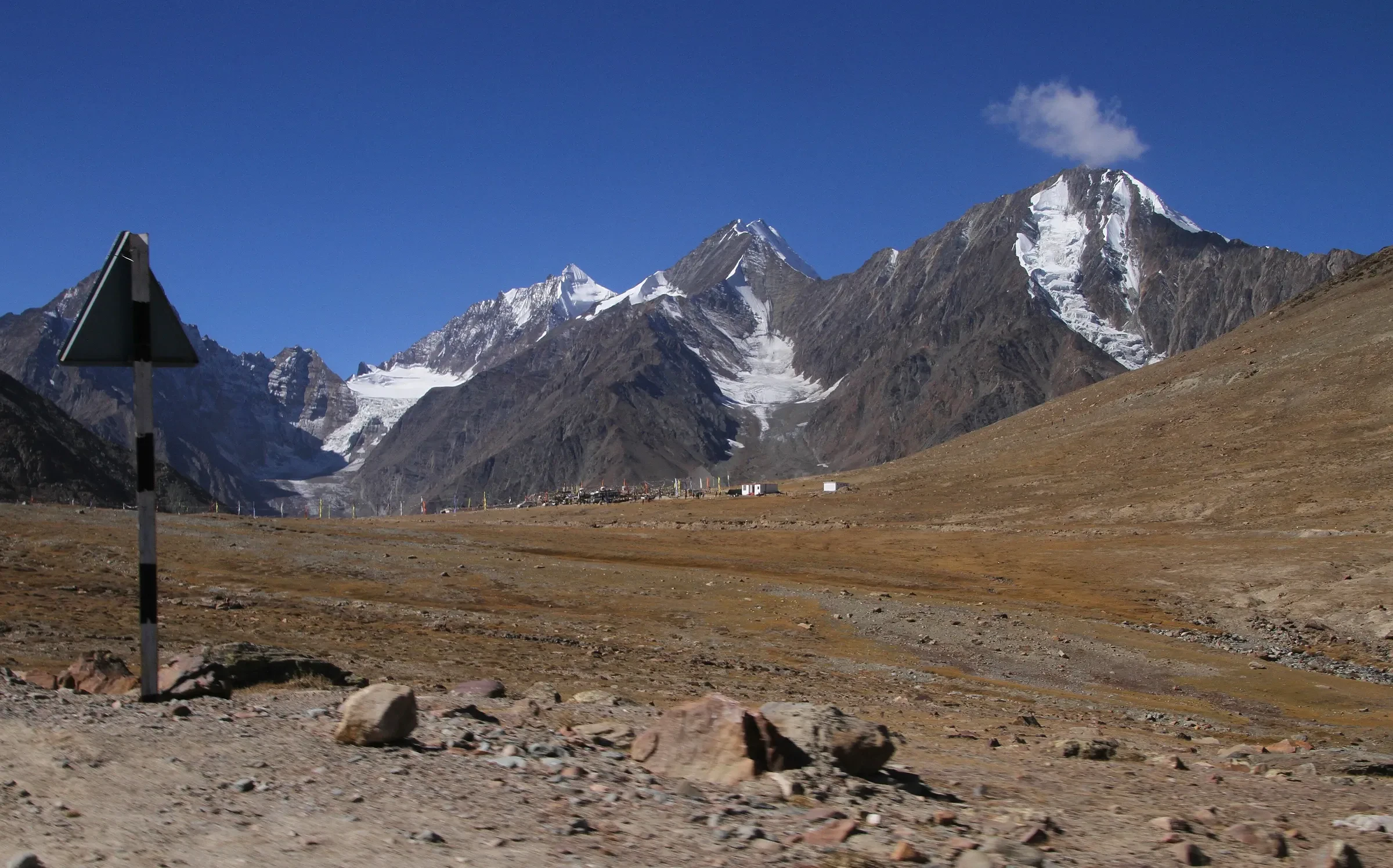 The Kunzum La pass top with snow peaks and a road sign post