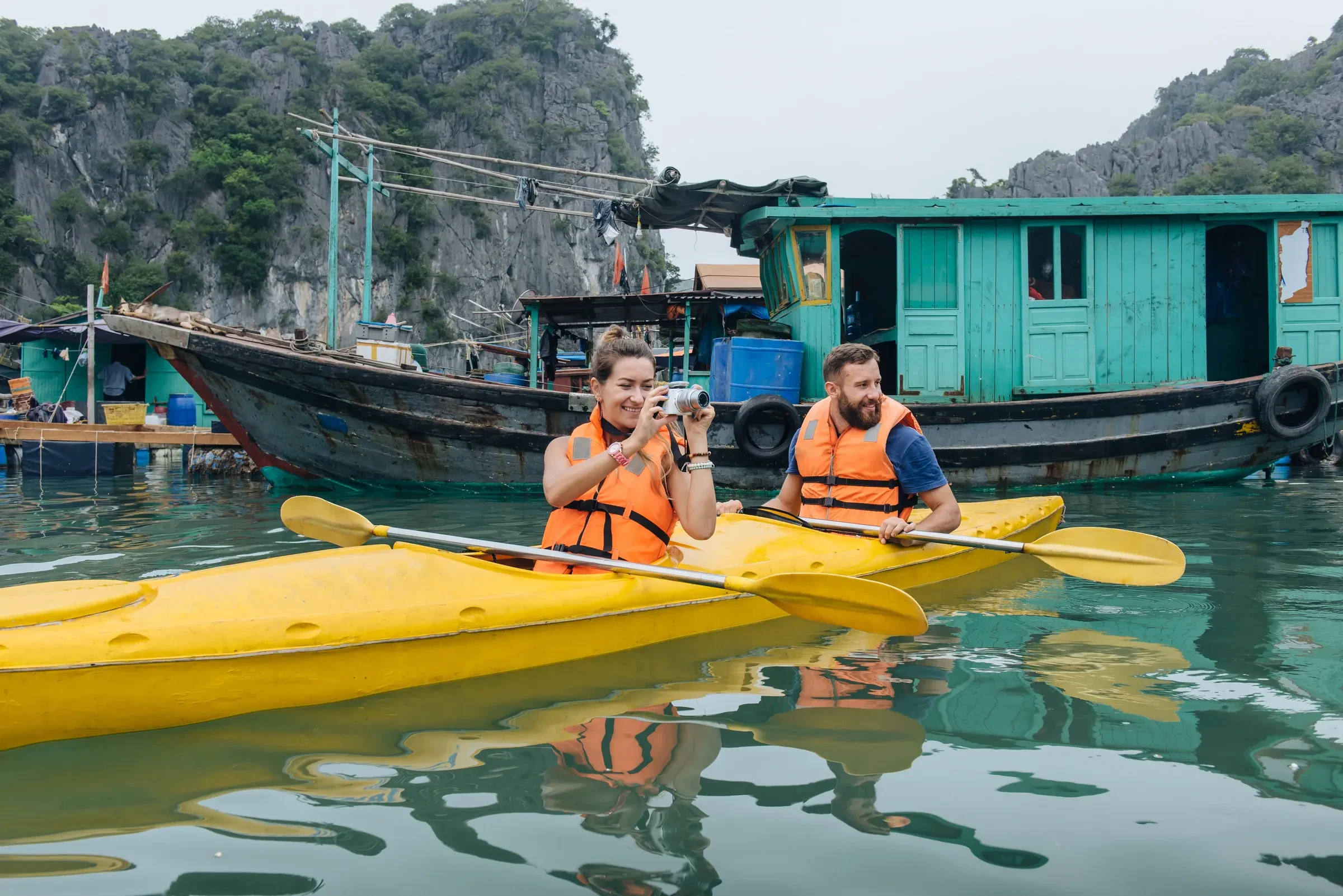 Two travellers in kayaks beside a floating fishing village in the bay off Cat Ba